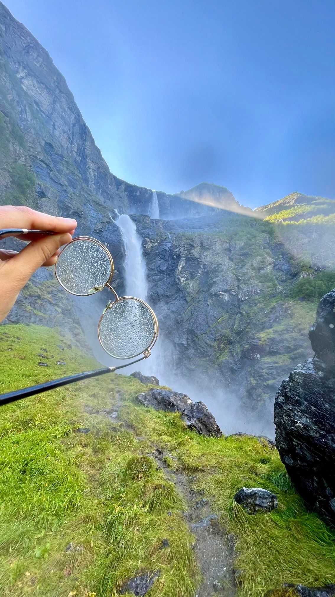 Des lunettes remplies de gouttes d'eau devant la cascade de Mardalsfossen